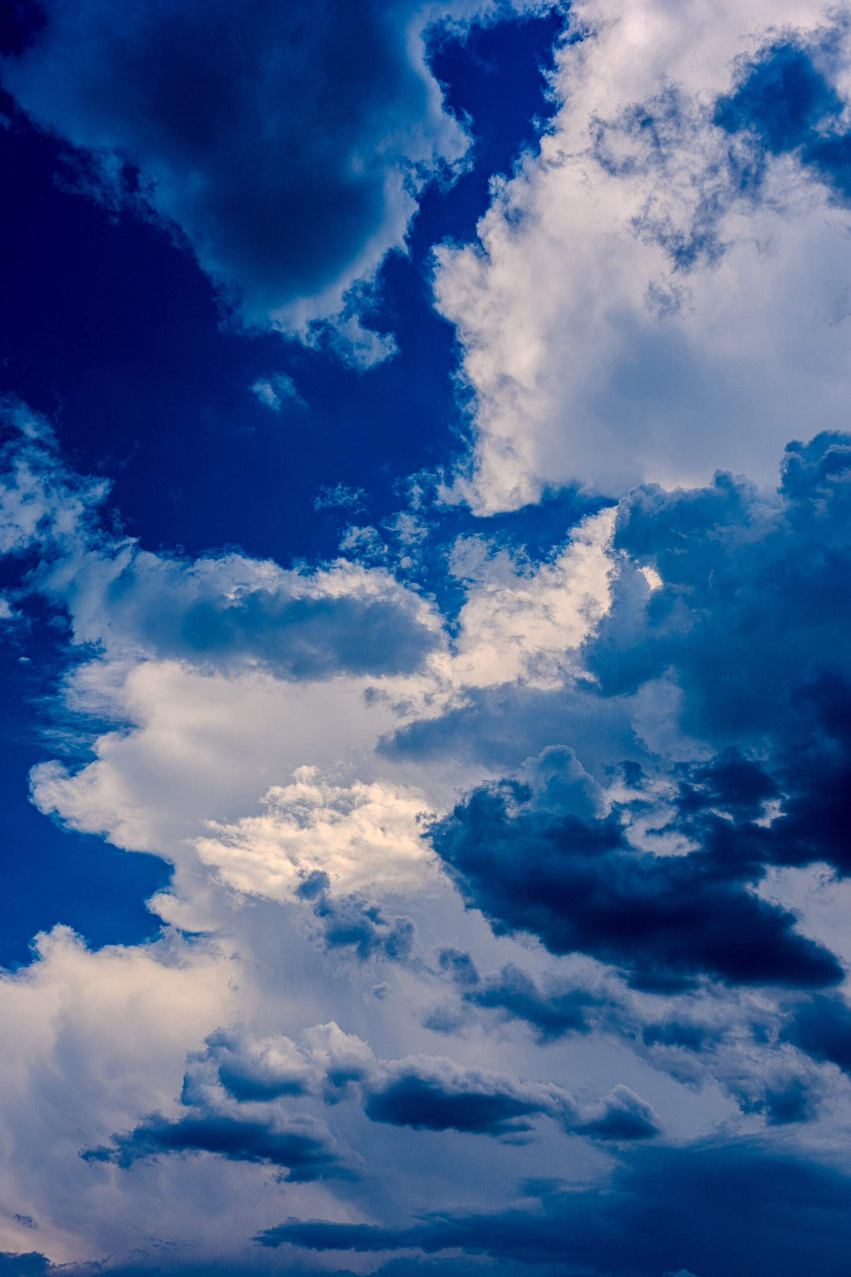 Dramatic cloudscape with bright sunlight breaking through dark storm clouds against a deep blue sky.