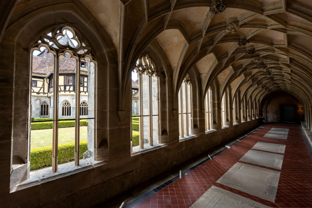 Gothic cloister corridor at Bebenhausen Abbey with vaulted ceilings, stone tracery windows, and views into the monastery courtyard.