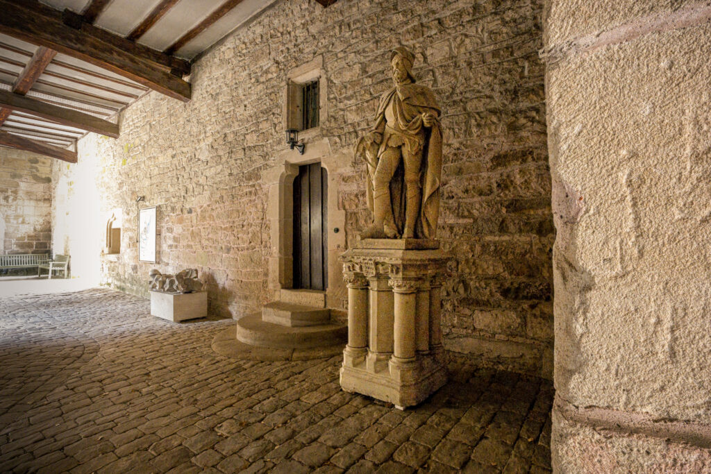 Historic stone statue inside Bebenhausen Abbey surrounded by medieval masonry, cobblestone flooring, and centuries-old monastery architecture.