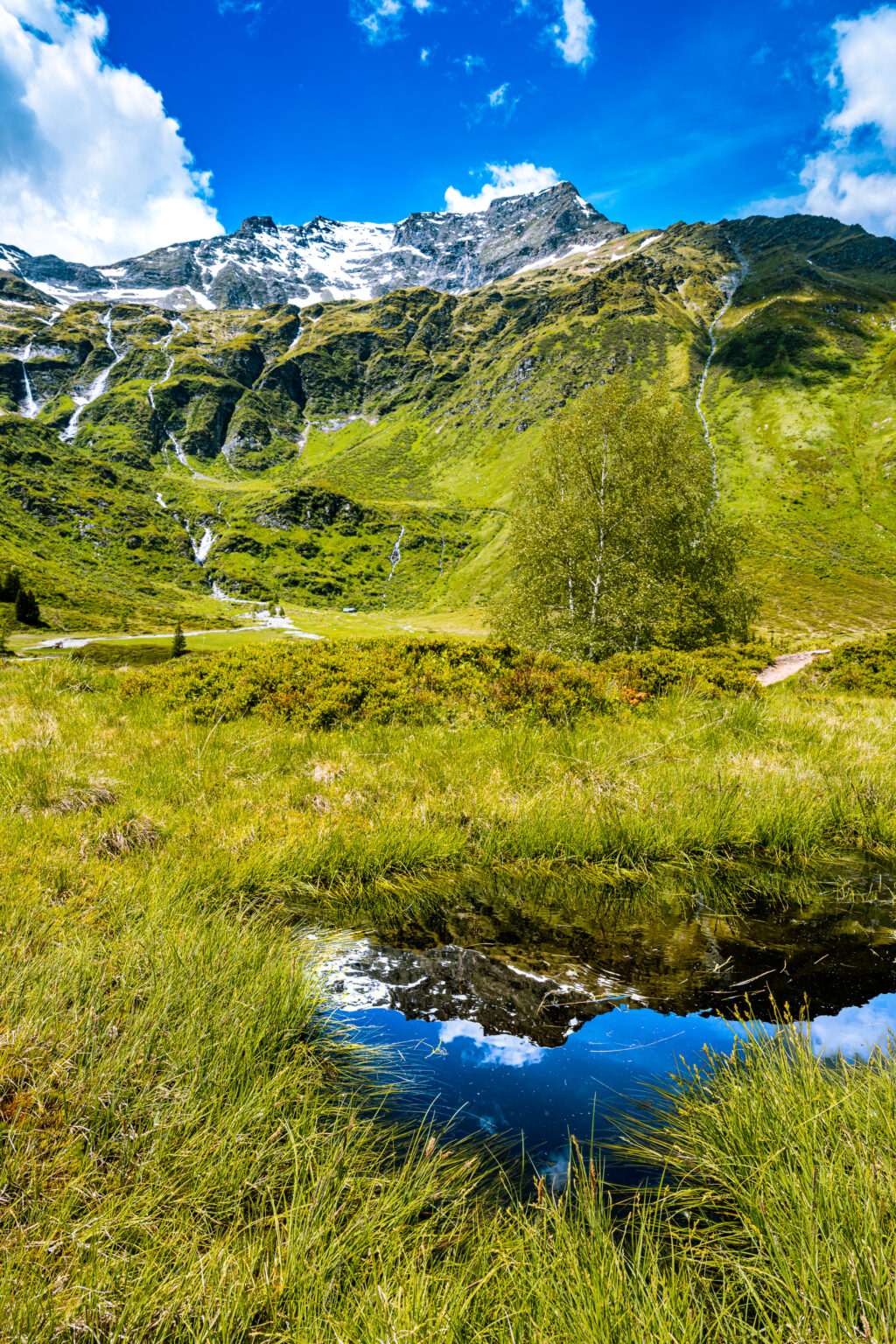 Reflection of snow-covered mountain peaks in a crystal-clear alpine pool in Sportgastein, Hohe Tauern National Park, Austria.