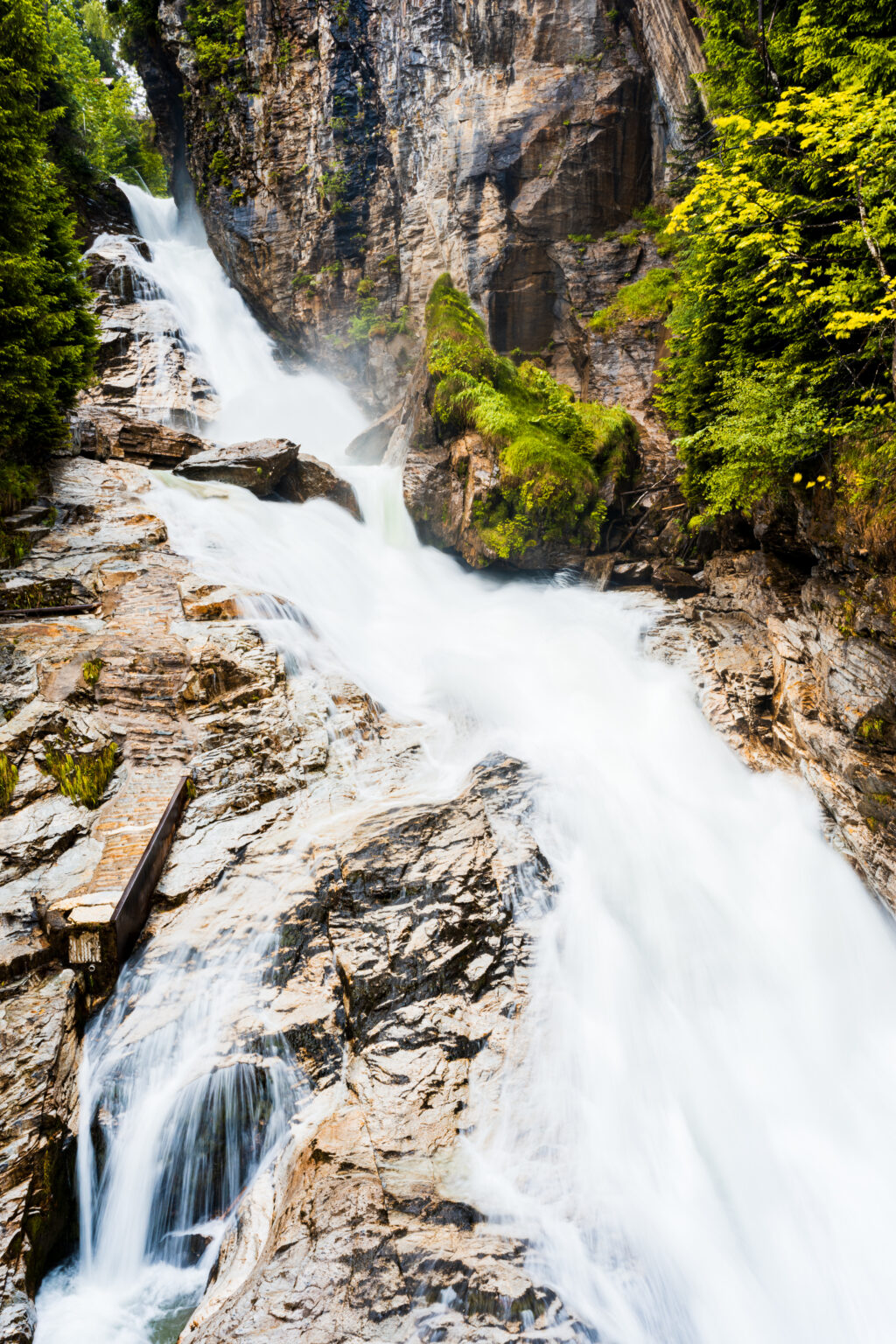 Close-up view of the Bad Gastein Waterfall flowing over rugged alpine rocks with lush green forest in Austria.