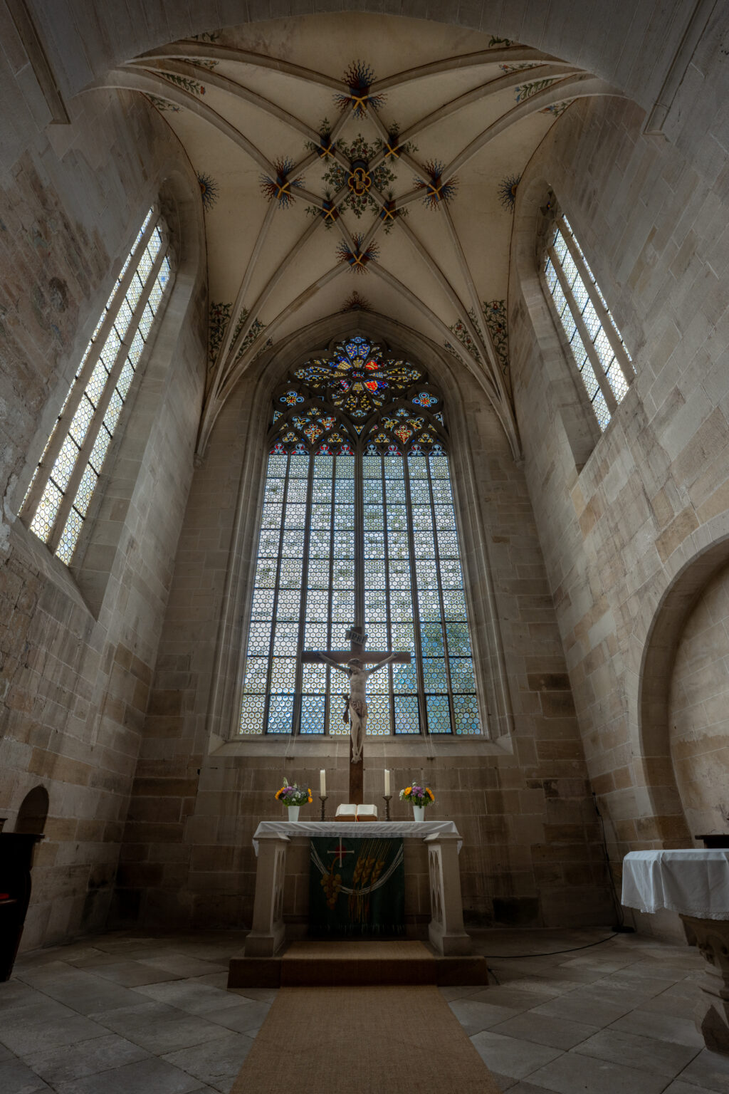Altar and Gothic stained glass window inside Bebenhausen Abbey church with vaulted ceiling and historic stone architecture.