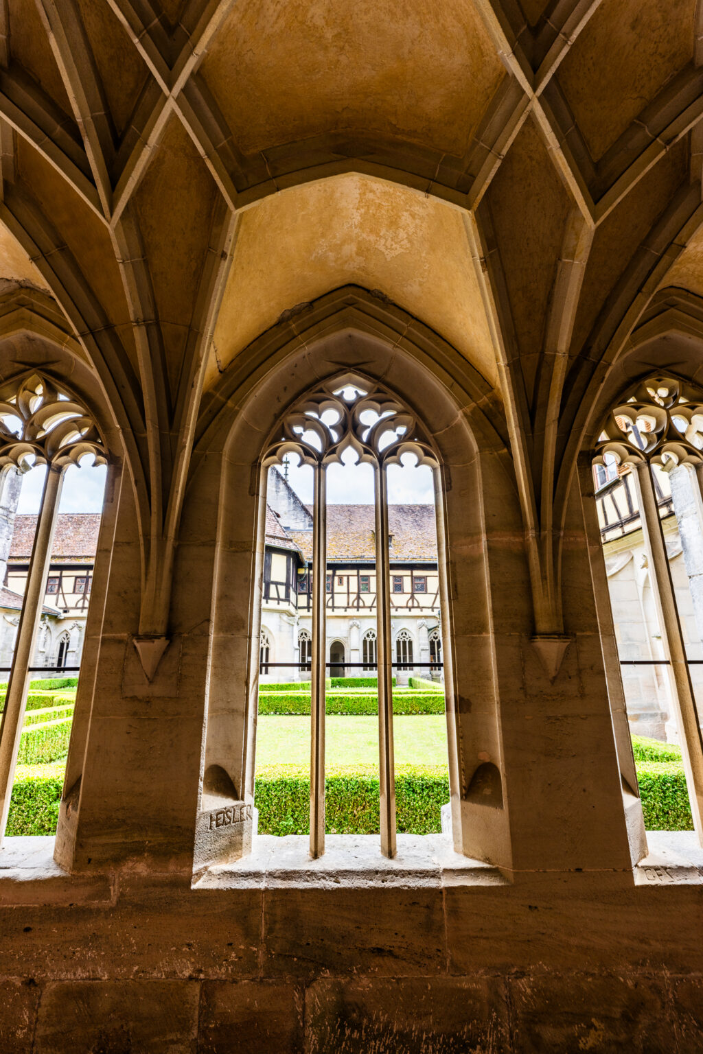 Gothic cloister window at Bebenhausen Abbey framing the monastery courtyard with medieval architecture and stone vaults.