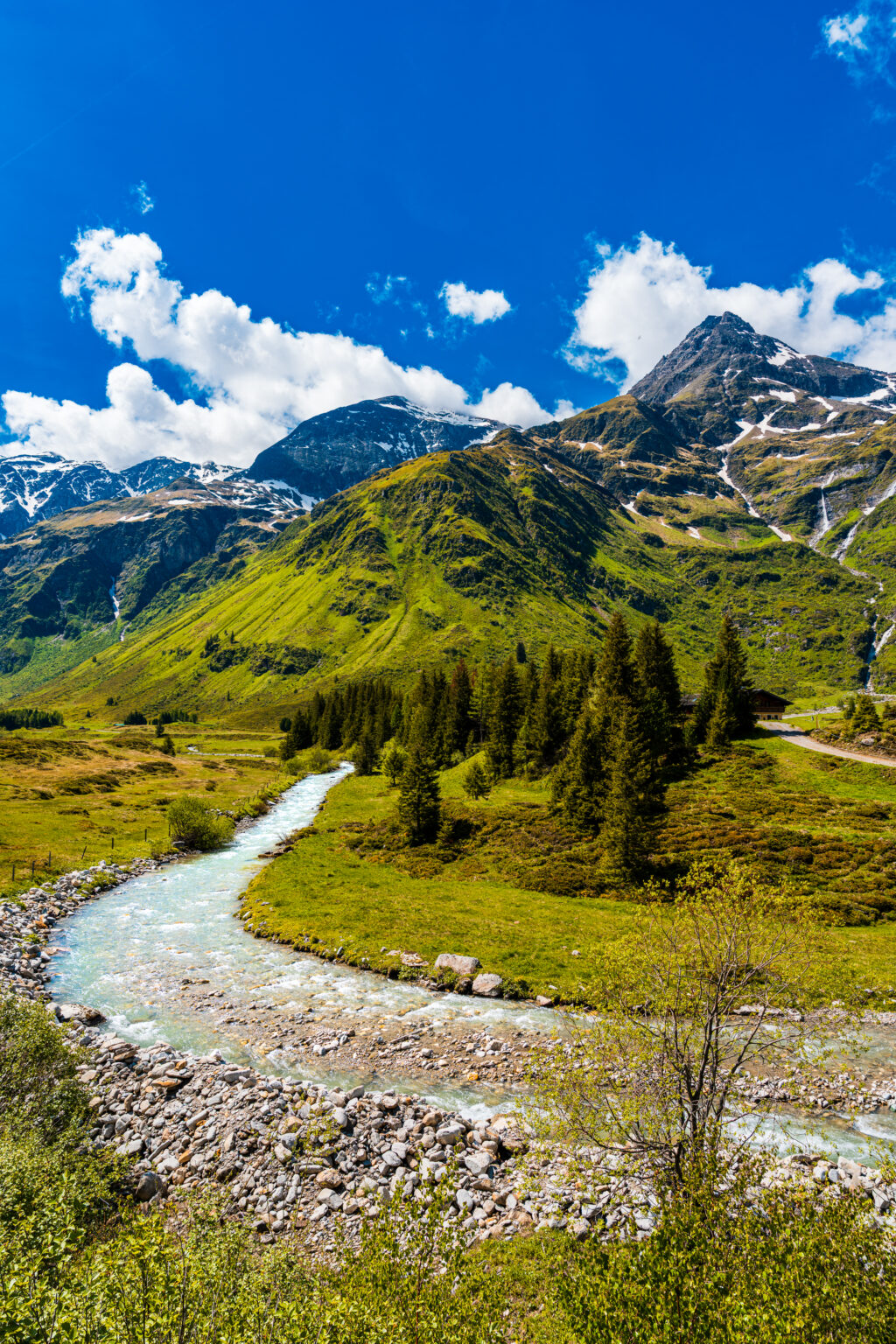 Crystal-clear mountain stream flowing through Sportgastein with alpine meadows and snow-covered peaks in Hohe Tauern National Park, Austria.