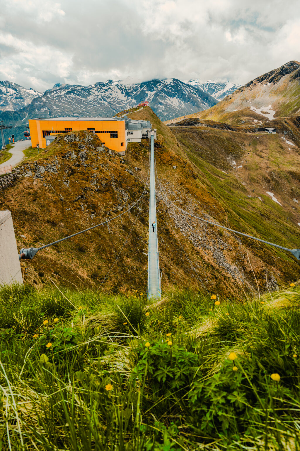 The 140-meter Stubnerkogel Suspension Bridge spanning above the Gastein Valley with the snow-covered Hohe Tauern Alps in the background.