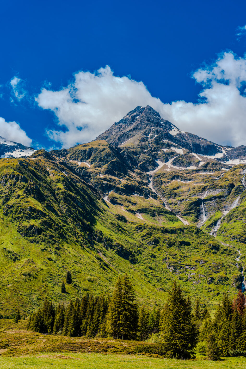 Majestic mountain peak rising above forests, waterfalls, and alpine meadows in Sportgastein, Hohe Tauern National Park, Austria.